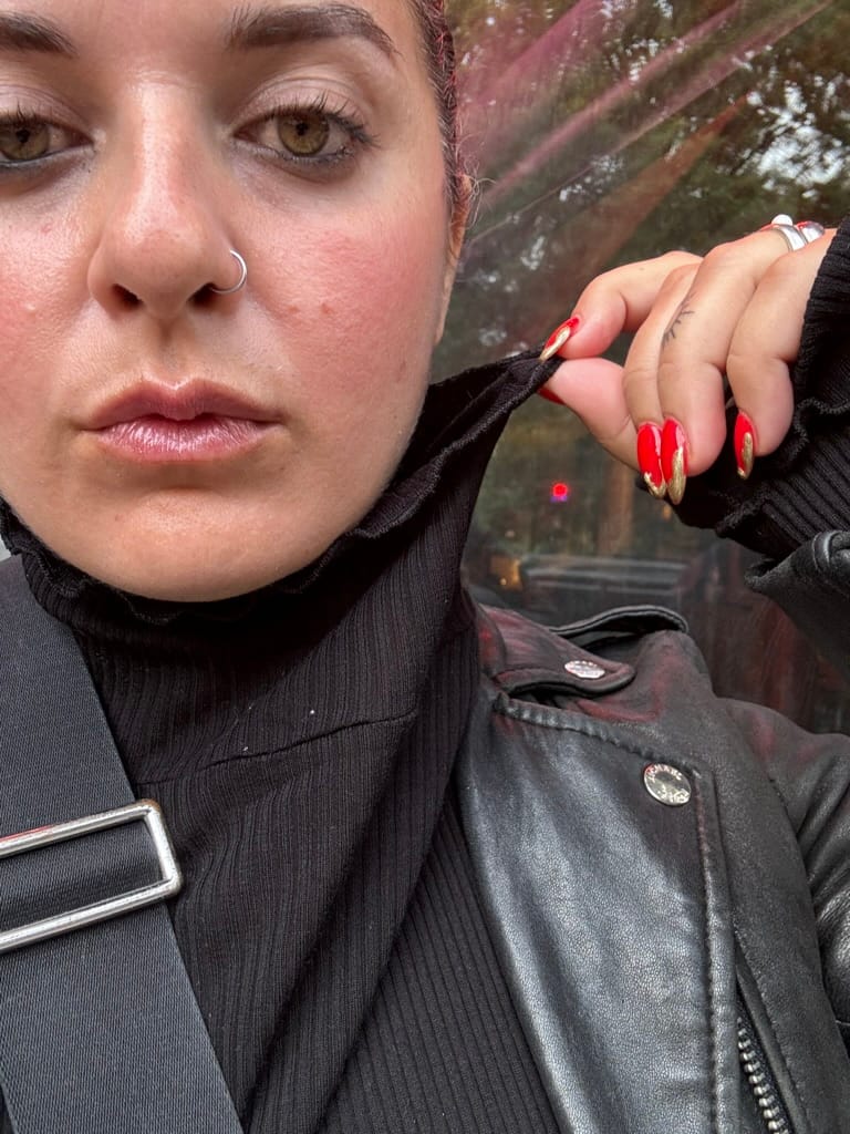 Alicia Kennedy takes a selfie wearing a black turtleneck and holding the collar with her bright red nails.