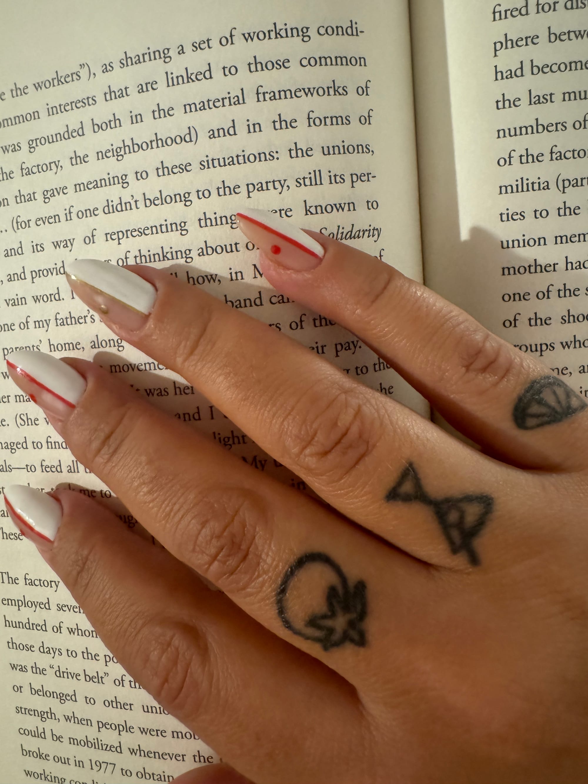 A selfie Alicia Kennedy took of her hand placed on an open book, showing simple line-art style tattoos of a martini, a tomato and an slice of citrus.
