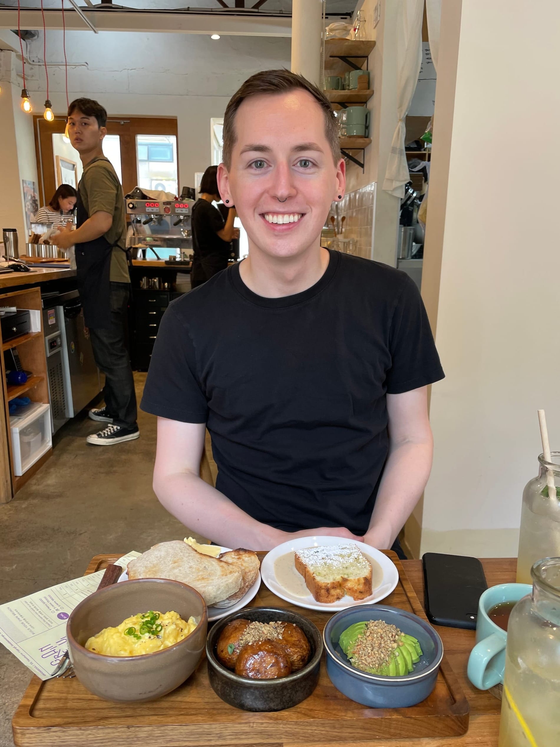 Paris Marx smiles at the camera, sitting in a restaurant with a full spread before him.